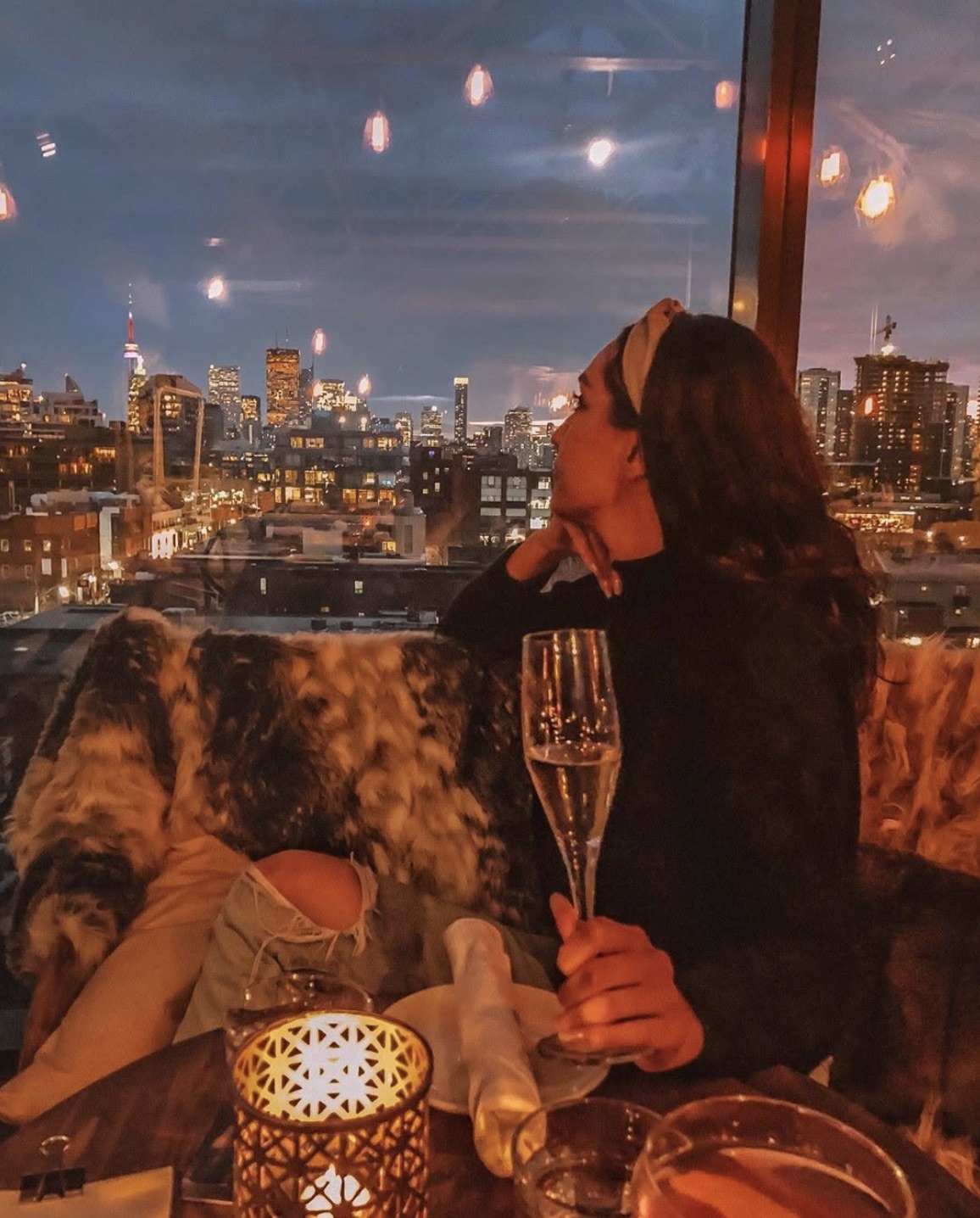 A guest with a glass of champagne on the Rooftop at night, the Toronto skyline glowing beyond